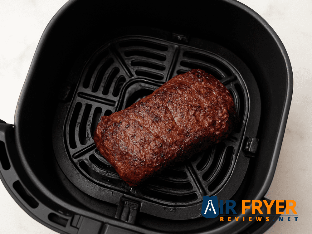 Steak cooking halfway in an air fryer basket, showing a brown seared crust.