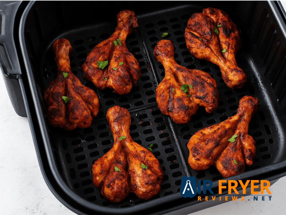 Butterflied chicken drumsticks cooking in a black air fryer basket Air Fryer Reviews