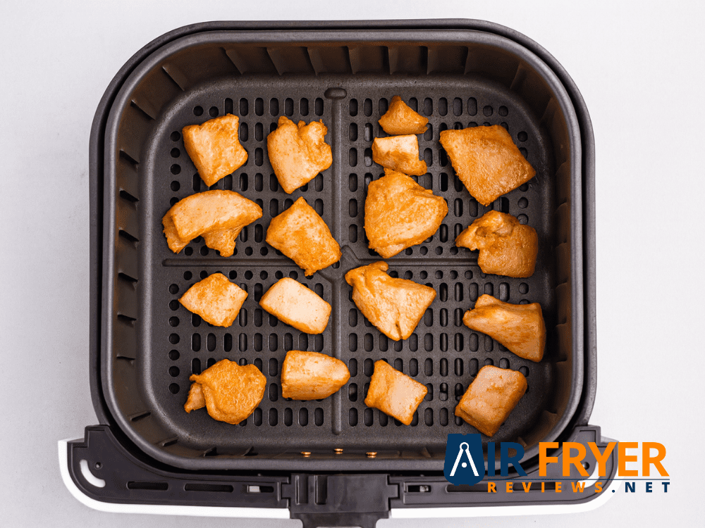 Raw seasoned chicken pieces placed in an air fryer basket.