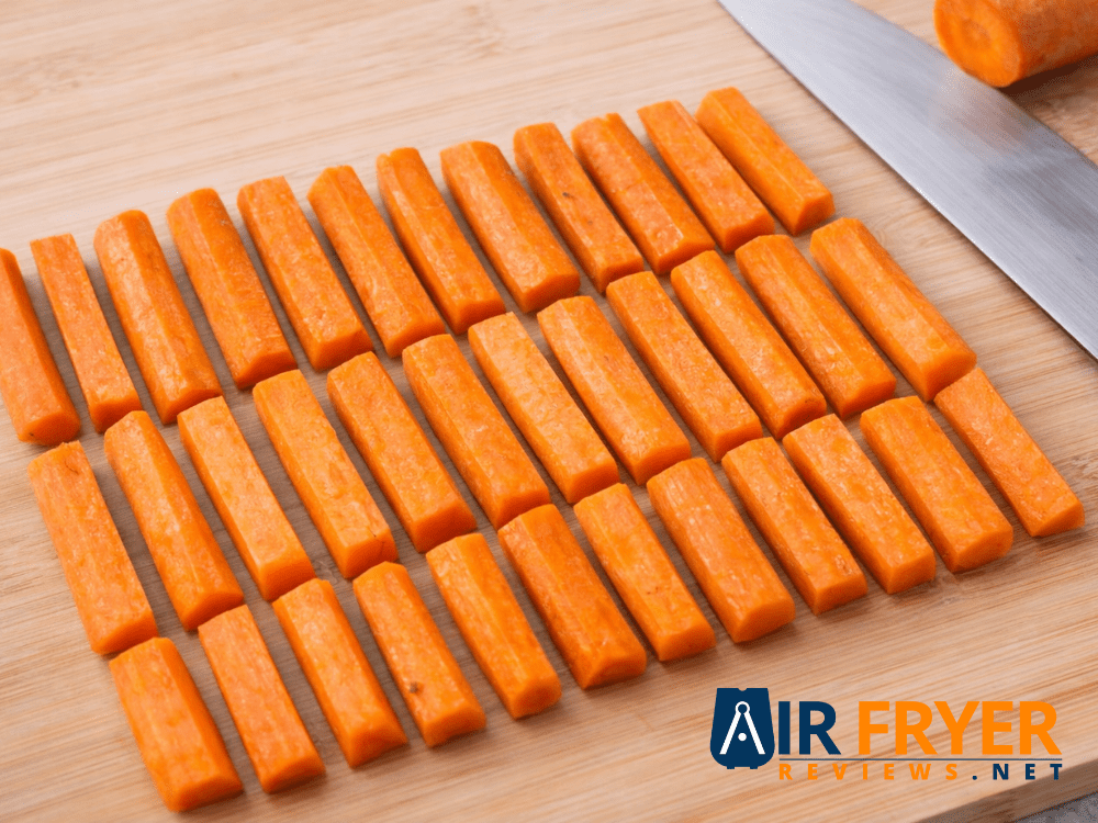 Carrots cut into evenly sized sticks arranged neatly on a wooden cutting board for uniform cooking Air Fryer Reviews