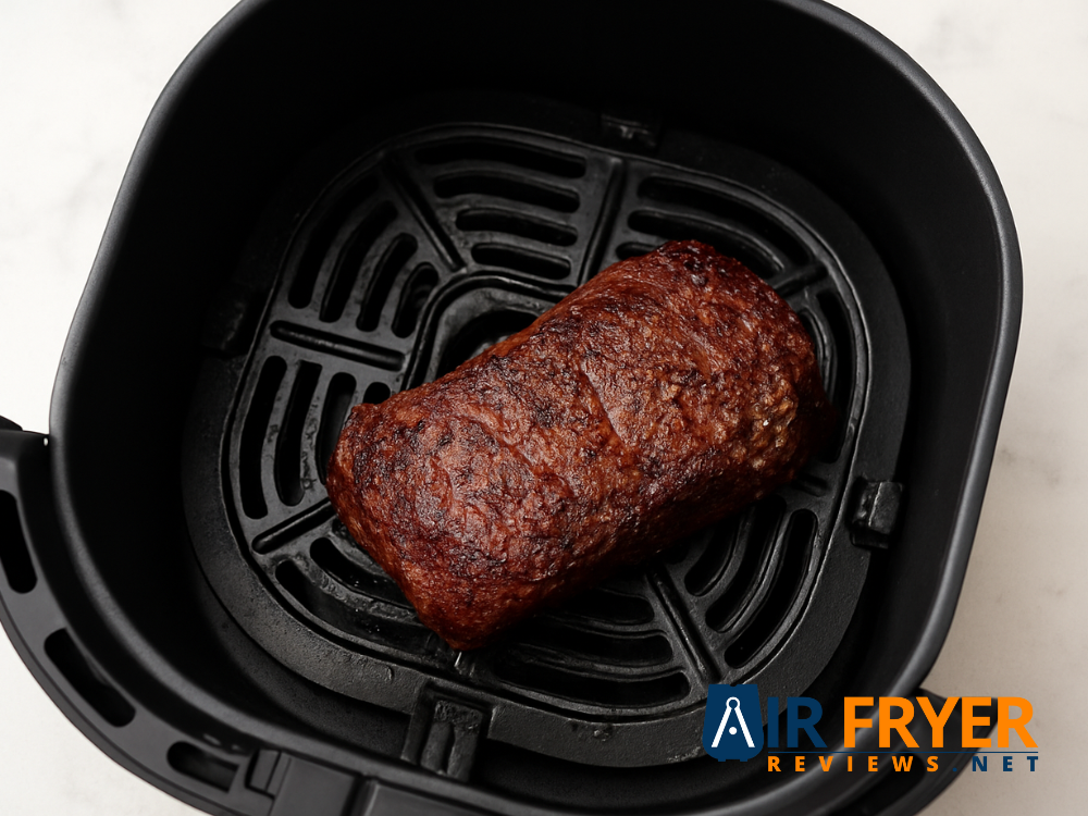 Steak cooking halfway in an air fryer basket, showing a brown seared crust.